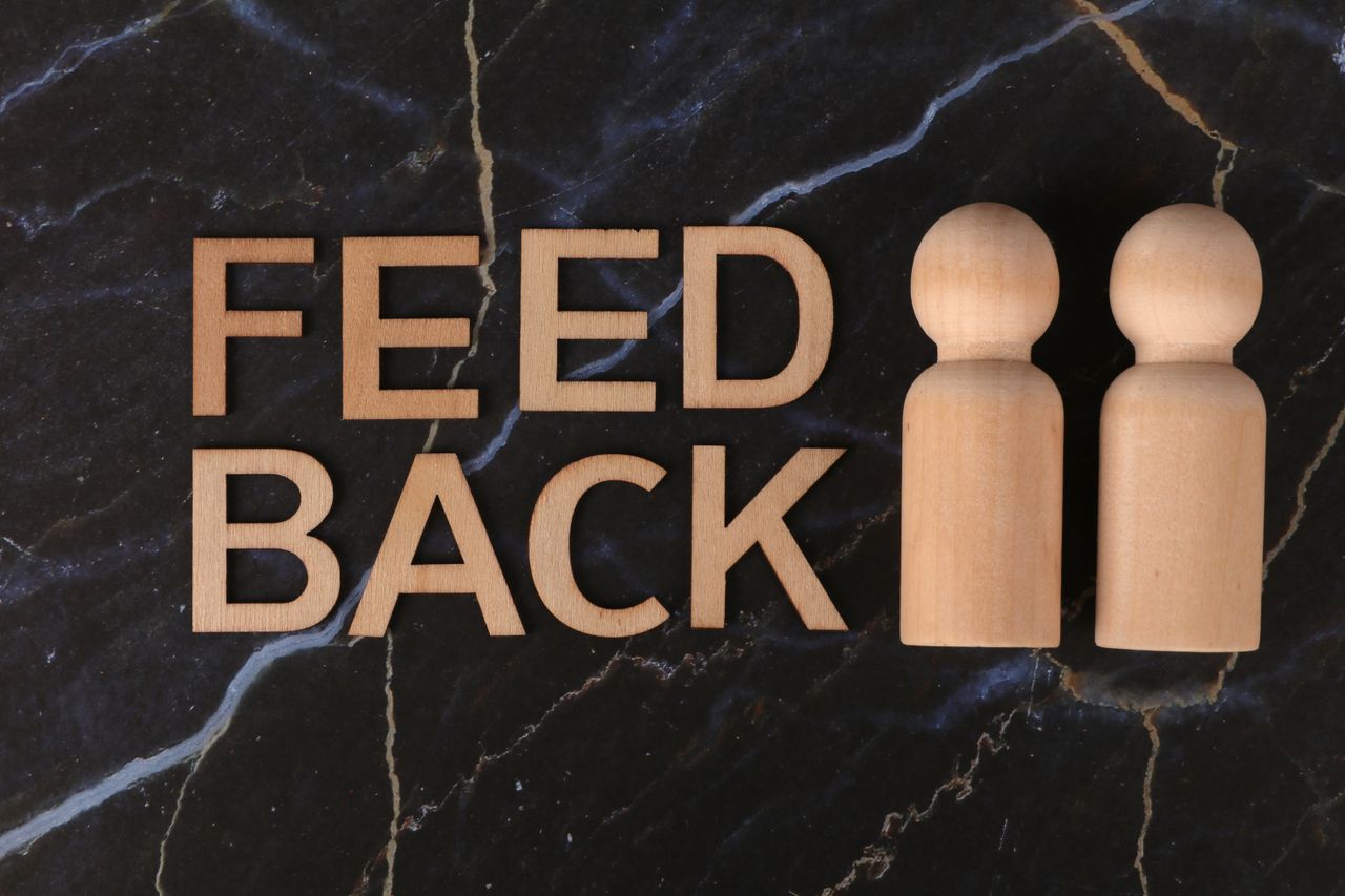 Offerings Wooden figures and 'feedback' text on black marble background, symbolizing communication and review.