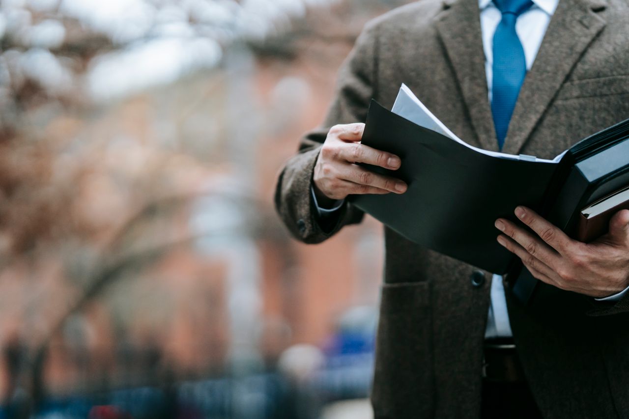 A professional in formal wear reviewing documents outside, showcasing business attire and focus.