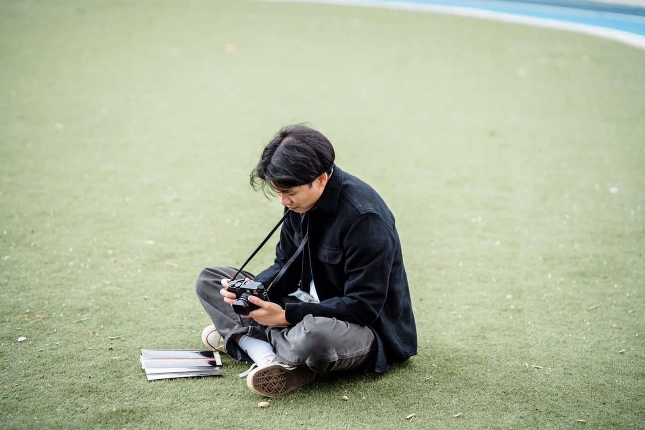 Offerings Young male photographer sitting on grass, examining camera screen for shots.